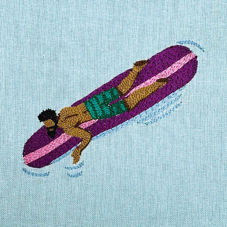 Embroidery of a person on a purple surfboard with green shorts on a light blue fabric background