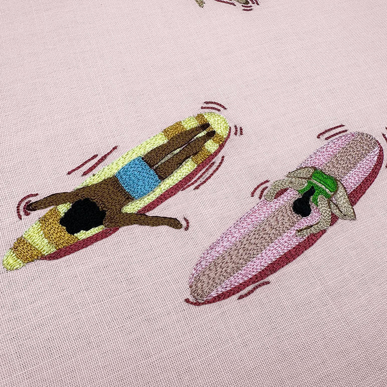 Embroidered design of a dog on a banana boat with another dog on a pink background