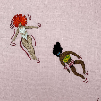 Embroidered design of two women in swimsuits on a pink fabric background