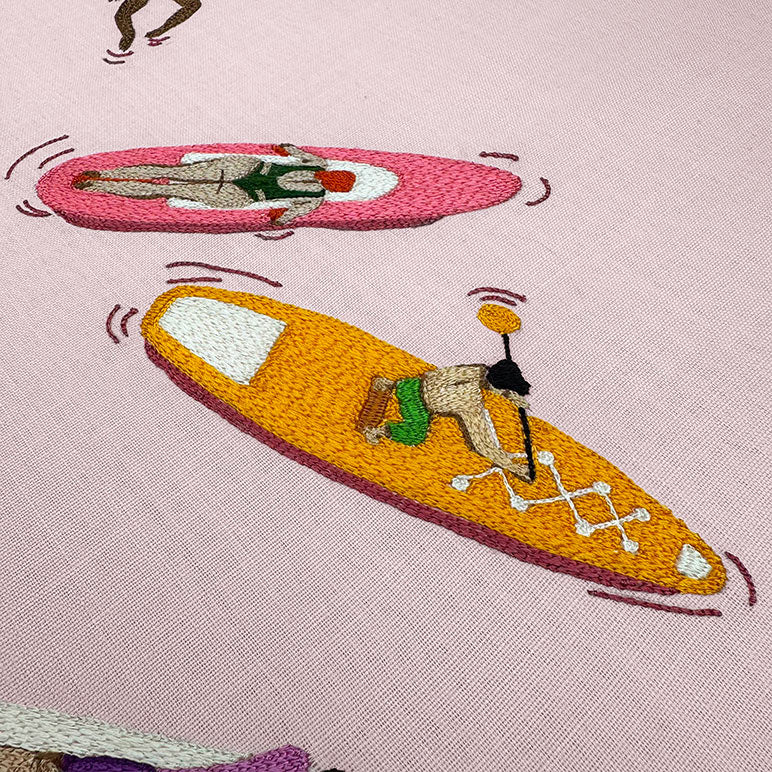 Embroidered design of a person on a pink surfboard and another on an orange surfboard with a pink background.
