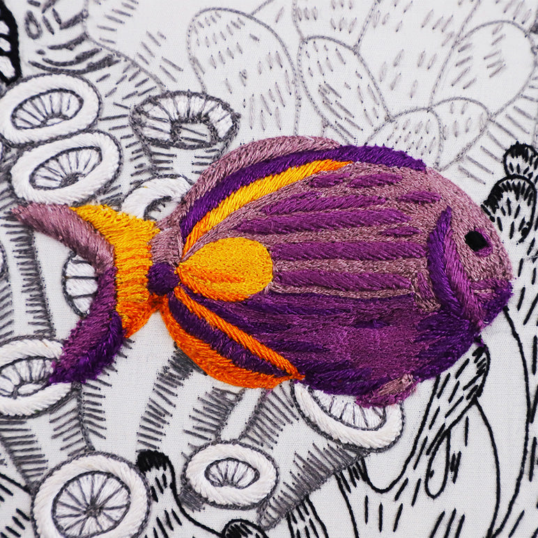 Embroidered purple and orange fish on a black and white patterned background