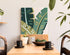 Decorative plant wall art above a wooden table with cups and a bowl.
