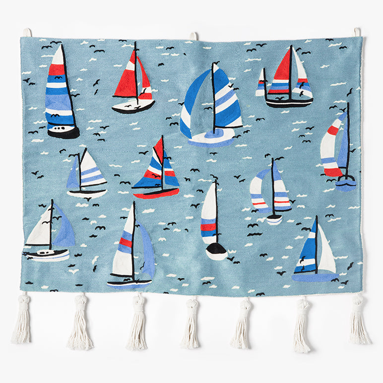 Hand-embroidered wall hanging with colorful sailboats on a blue sea, finished with white tassels on a white background