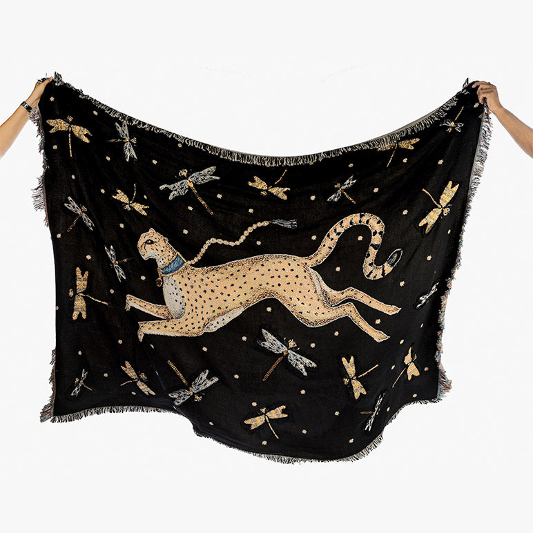 Black beaded throw blanket with a cheetah and dragonfly design held by two hands against a white background