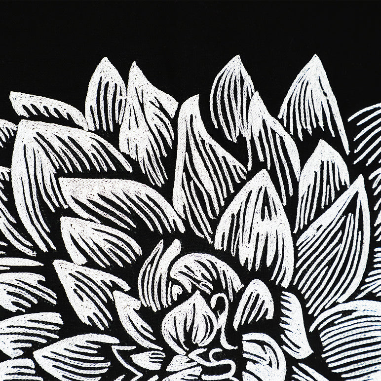 Close-up of an embroidered wall hanging with black and white floral pattern of succulent leaves on a black background