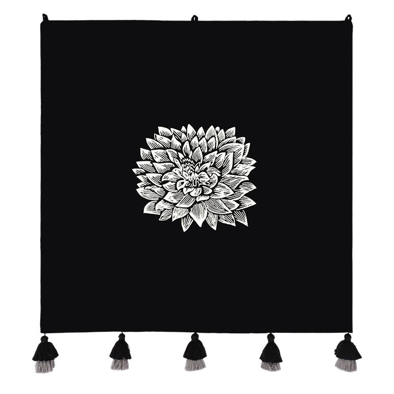 Black floral wall hanging with a white floral design and tassels on a white background