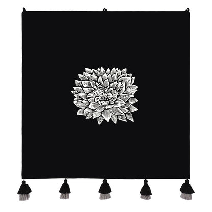 Black floral wall hanging with a white floral design and tassels on a white background