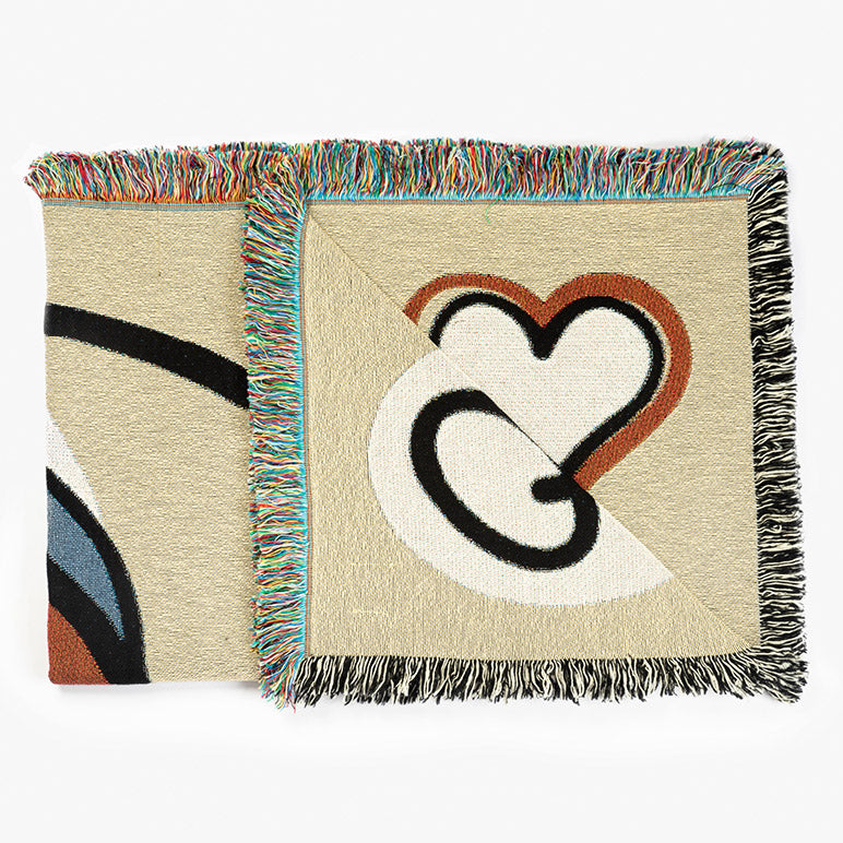 Folded designer throw blanket with a heart design and colorful fringe on a white background