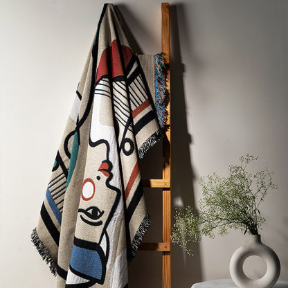Colorful abstract designer throw blanket draped over a wooden ladder against a neutral wall with a vase of flowers on a surface.