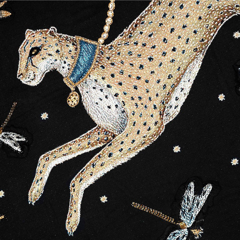 Embroidered cheetah design on a black throw blanket with decorative elements.
