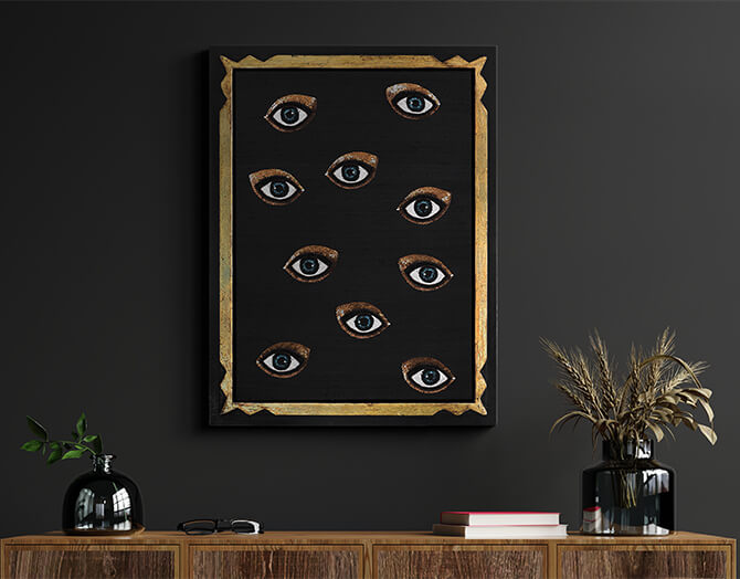 Framed artwork with eyes on a dark wall above a wooden console table.