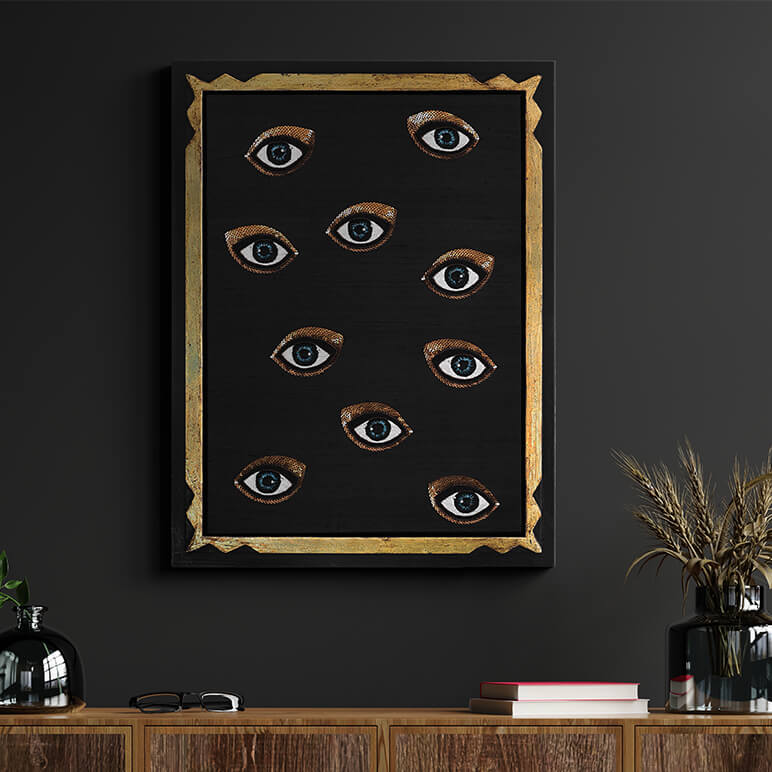 Framed artwork with eyes on a black background in a room with a wooden cabinet and decorative items.