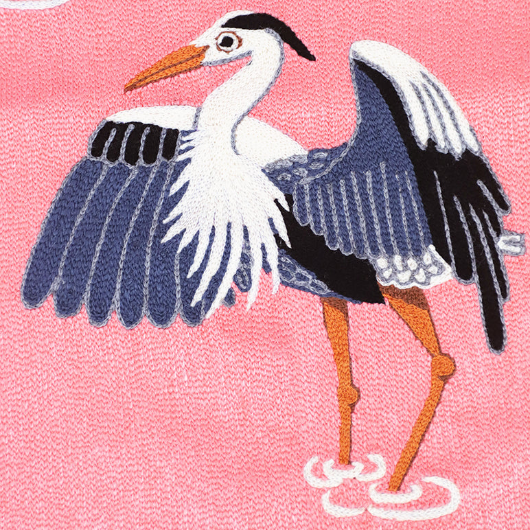 Close-up of Herons nursery wall art—hand-embroidered heron with spread wings in navy, white and black on a bright pink background, orange beak and legs with stitched water ripples.