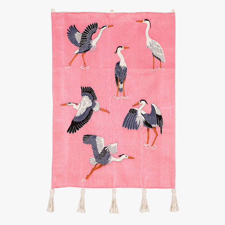 An embroidered wall hanging featuring navy-and-white herons on a pink ground with ivory tassels; ideal for kids’ room décor.