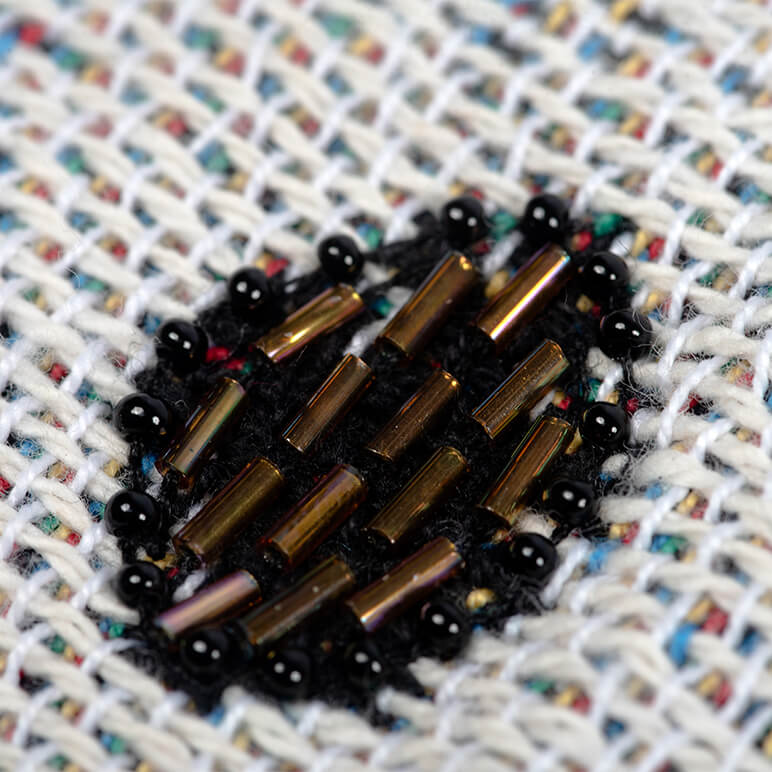 Close-up of a beaded heart-shaped object on a textured fabric background