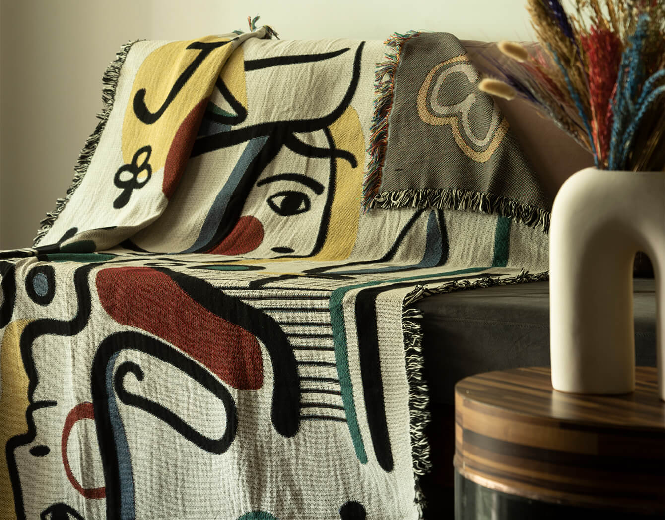 Abstract patterned blanket draped over a sofa with a vase in the background
