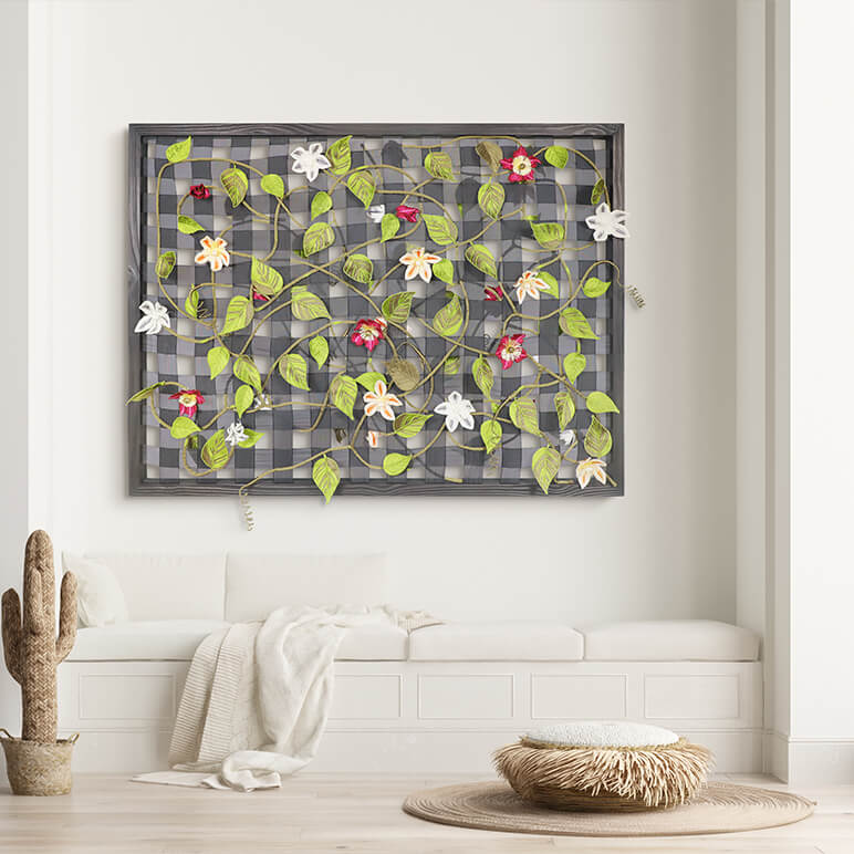 Decorative wall art with floral patterns on a checkered background in a room with a white bench and cactus.