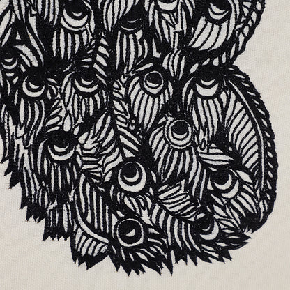 Close-up of hand-embroidered peacock feather motif in black thread on off-white embroidered wall hanging