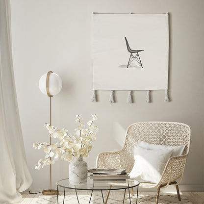 Embroidered wall hanging—minimal black chair on off-white textile with tassels—styled in a bright modern living room with cane chair and floor lamp; modern textile wall art.
