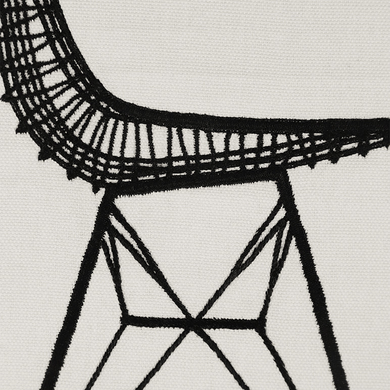 Close-up detail of “Sit Pretty” embroidered wall hanging—black stitched chair lines and geometric base on off-white cotton textile.