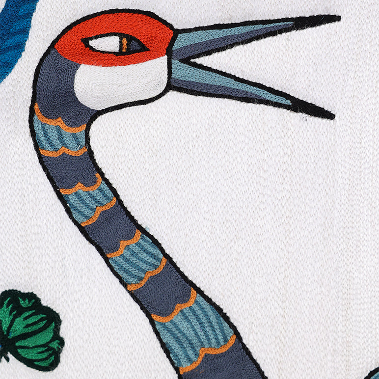 Close-up of *Songs of the Crane* embroidered wall hanging—detail of a crane’s head and striped neck in teal, navy and rust on ivory textile.
