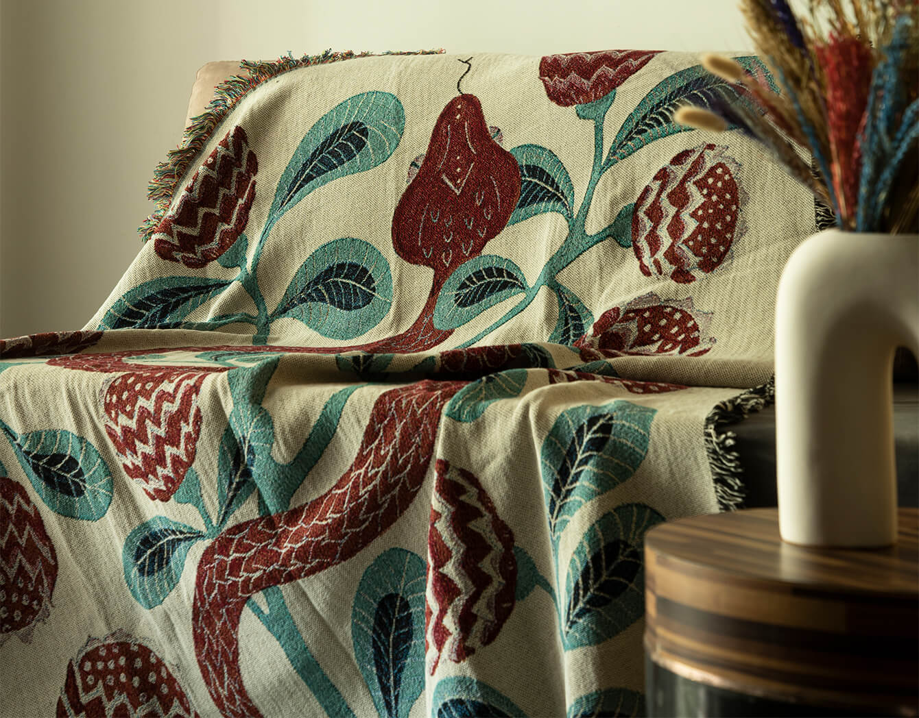 Decorative blanket with snake pattern draped over a surface, with a vase and dried plants in the background.