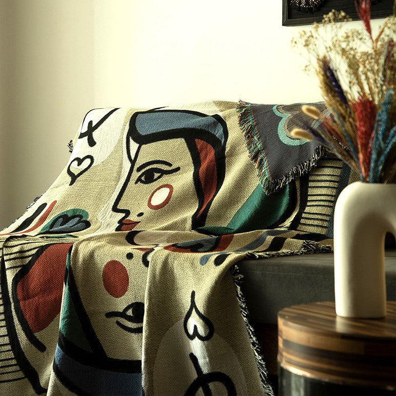 Decorative blanket with artistic design draped over a couch, with a vase of dried flowers in the background.