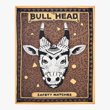 framed 3d textile wall art showcasing an enlarged vintage matchbox crafted using metallic embroidery to form a sculpted bull's head decorated with ornaments, seen over an earthy brown suede fabric. Has the titles "Bull Head" and "safety matches" al
