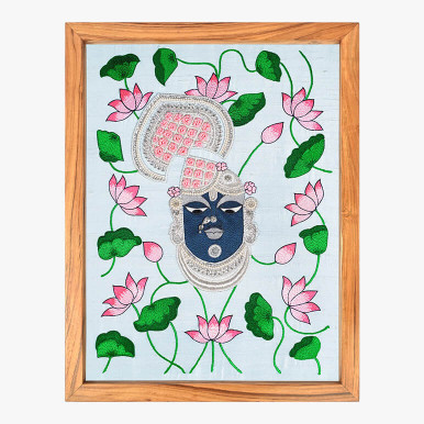 Feature image of a textile artwork showcasing Lord Shrinathji from the Nathdwara Shrinathji mandir, embroidered in jewel tones over a blue pastel fabric and framed in wood