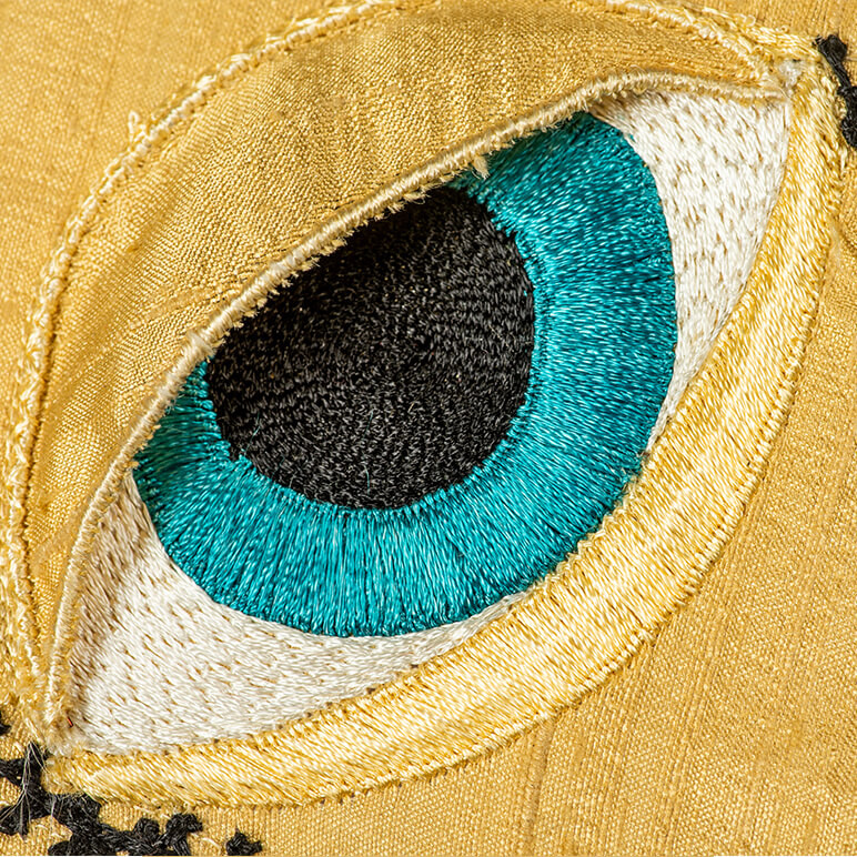 embroidered blue eye with a golden eye lid made in fabric and thread