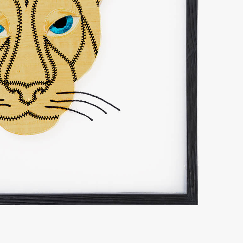 framed corner detail of an animal wall art with a golden panther head with blue embroidered eyes