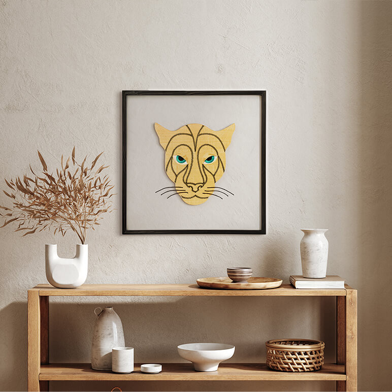 framed textile art featuring a golden panther head with black thread detailing displayed in a boho room