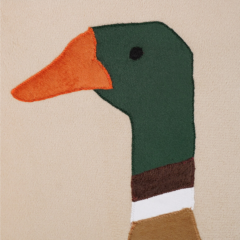 Close up view of the embroidery detail on an animal themed nursery decor piece showing a green duck over a beige background