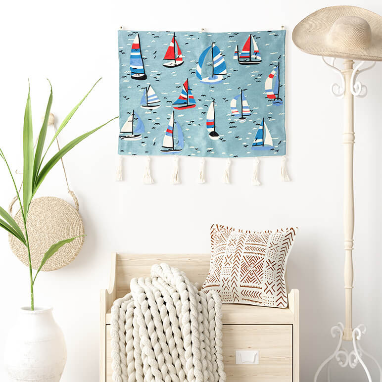 embroidered blue tapestry featuring sailboats on a blue sea seen displayed in a white room