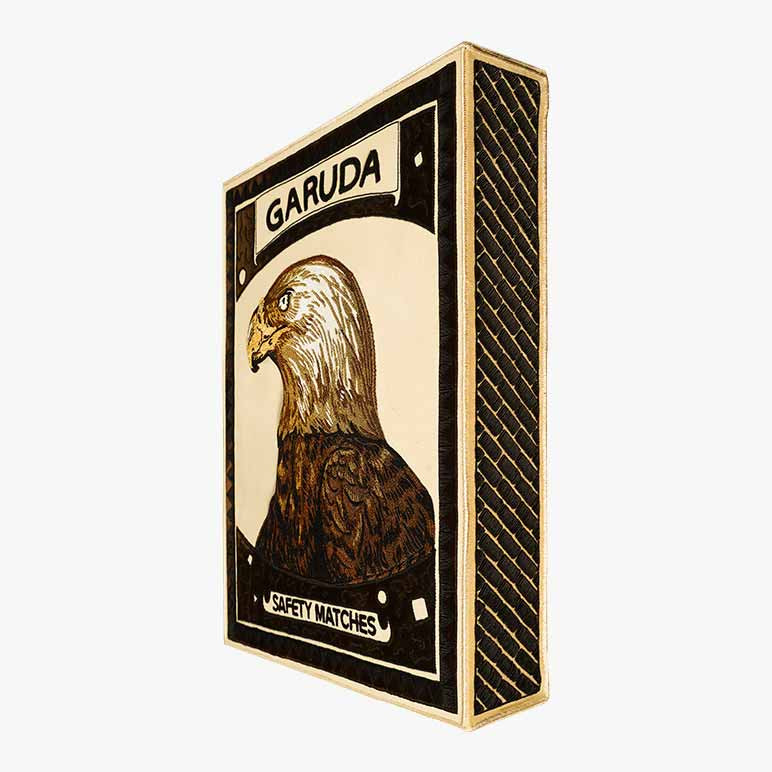 side angle view of a matchbox like textile sculpture featuring a bald eagle art at the top and the striking surface of a matchbox on the side, handcrafted using French purl wire
