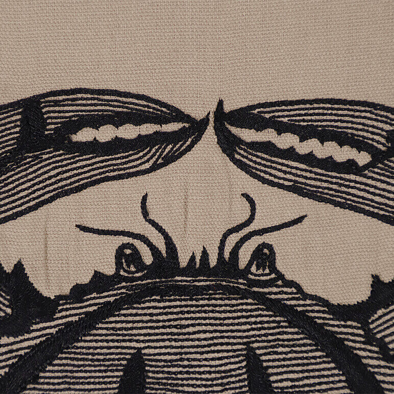 close-up view showing the black embroidery detail of a blue crab over a brown cotton background