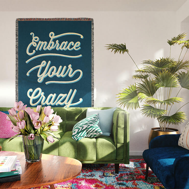blue throw blanket with the phrase embrace your crazy woven on top seen displayed on the wall of a bohemian living room
