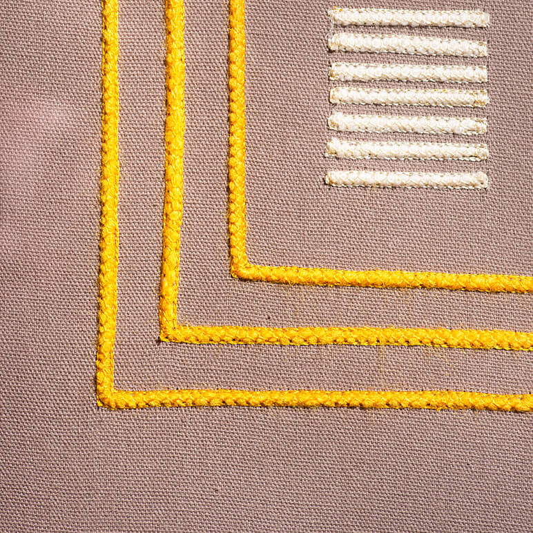 closeup view of the embroidery detail of a chic textile wall art in earthy colors
