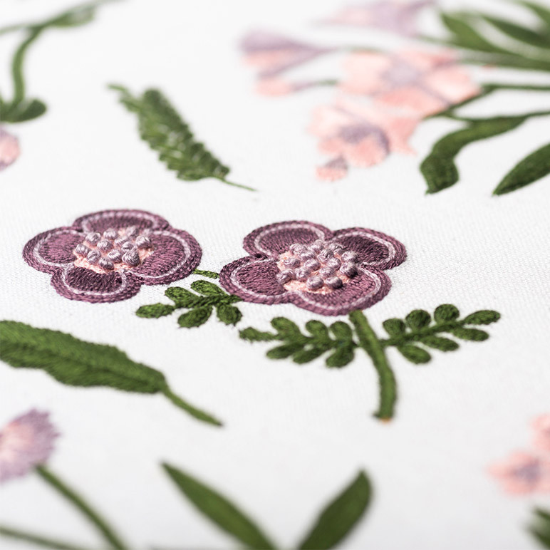closeup embroidery detail of a pastel purple colored floral textile art on a white cotton background