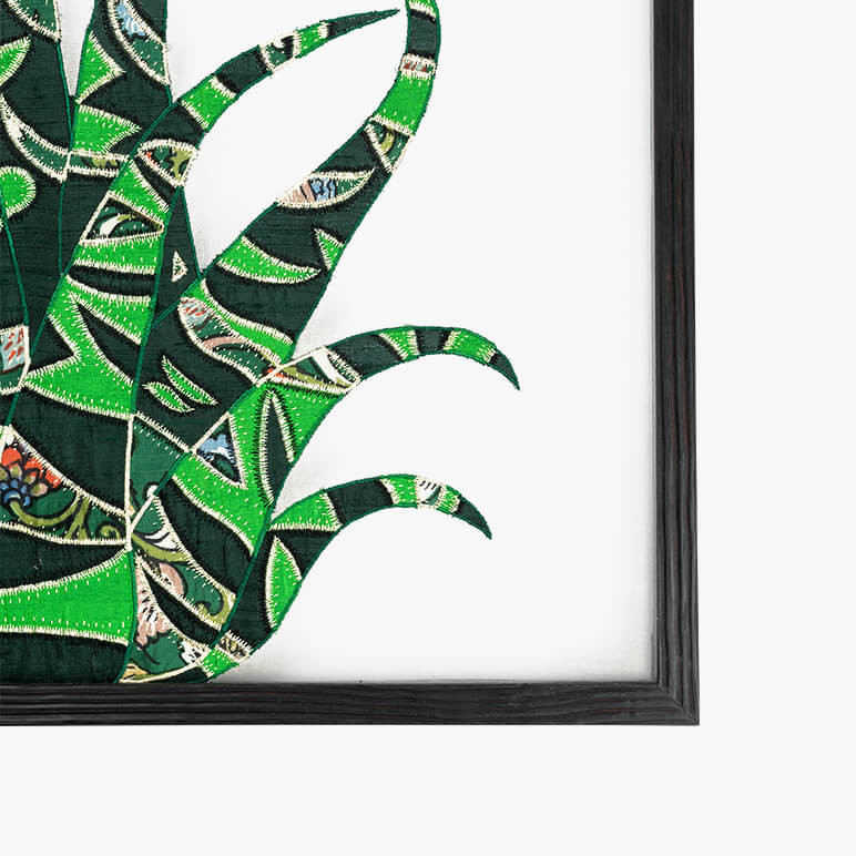 corner view of a framed textile artwork featuring a patchworked cactus in green colors