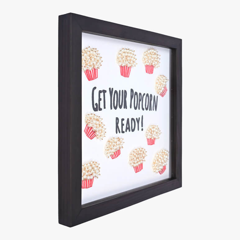 Left angle view of a typographical artwork that says get your popcorn ready, with embroidered popcorn motifs 