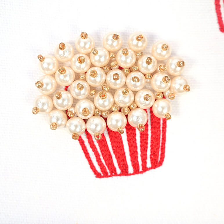 Close up detail of an embroidered popcorn bucket, in pearls, red and white colours