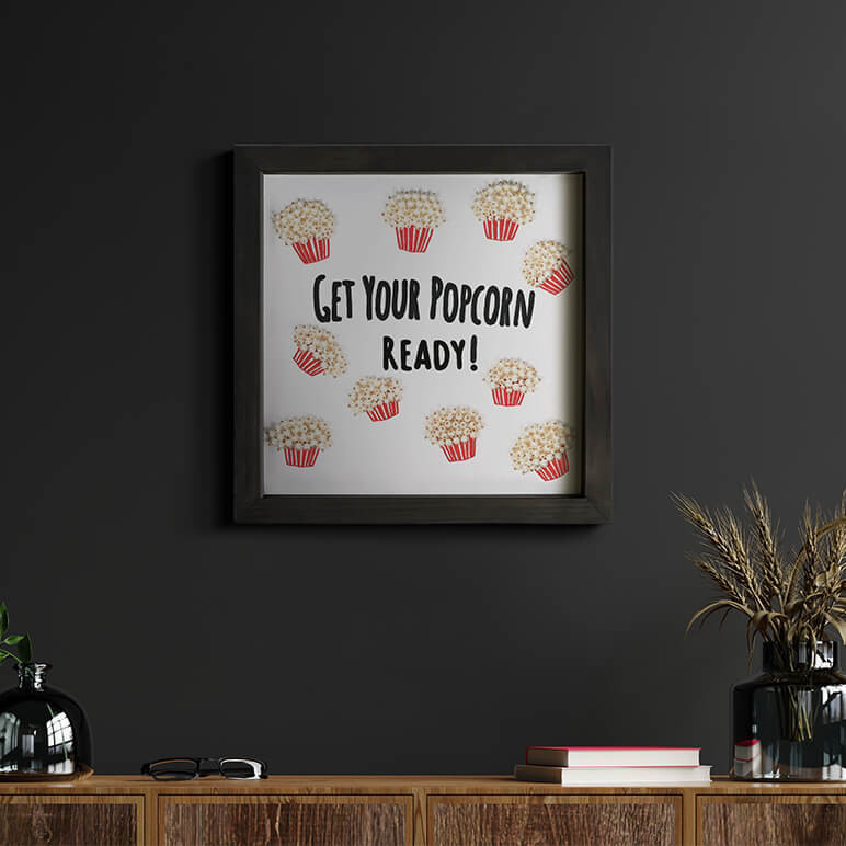 Staged view of a fun typographical artwork that reads get your popcorn ready, seen displayed in a dark walled room
