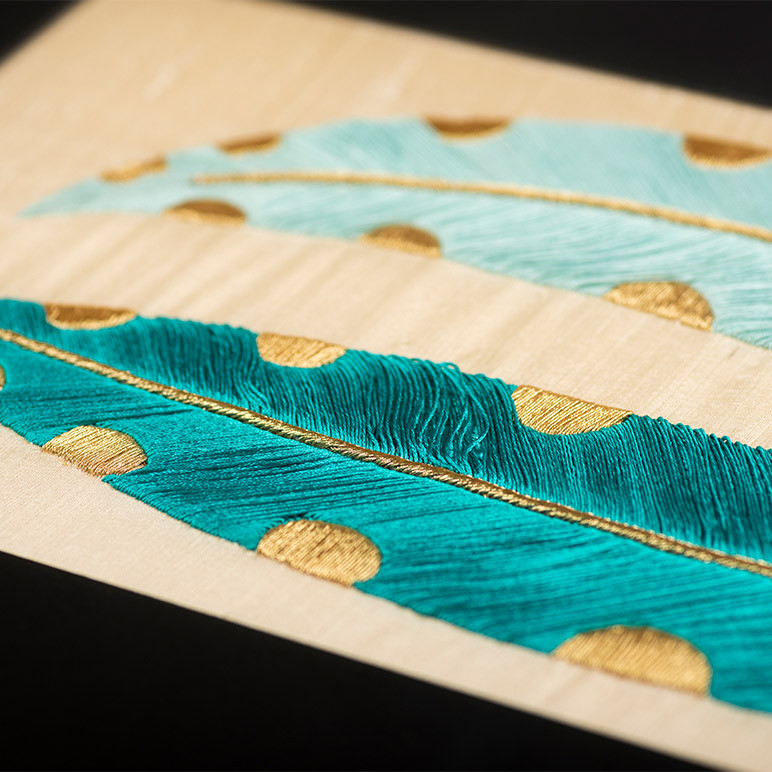 closeup embroidery detail of a teal and gold colored feather