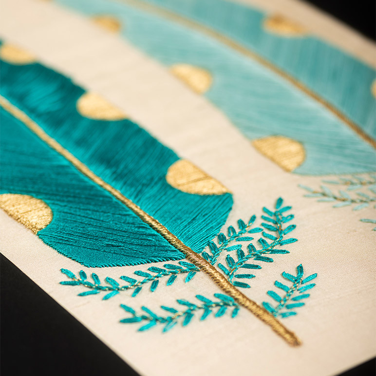 embroidery detail of a teal and gold colored feather in a textile artwork