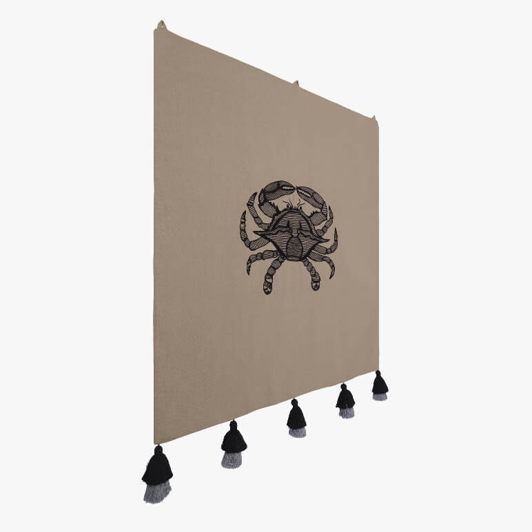 side view of a minimalistic crab wall art done in black thread work over an earthy toned cotton background, seen with five black tassels at the bottom