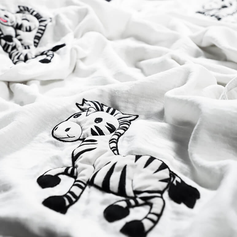 closeup view of a cute zebra blanket with embroidered zebras over a white bamboo cotton fabric