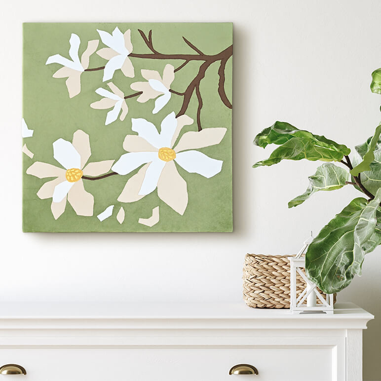 Floral wall art of a green and white colored patchworked textile art, canvas framed and displayed on a white wall over a white console table