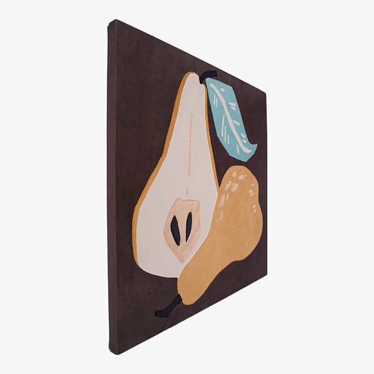 Left angle view of a canvas framed and earthy colored textile artwork featuring a golden pear cut in half