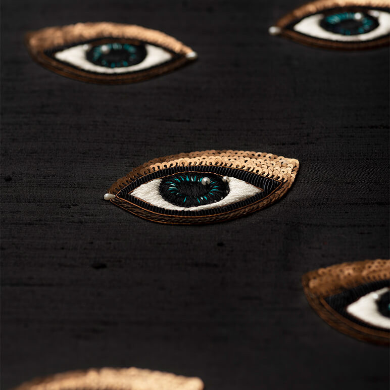 embroidery detail of a sequined eye over a black silk background